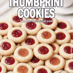 A plate of timeless thumbprint cookies filled with raspberry and apricot jam, served on a white marble tray with a cup of coffee in the background.