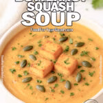 A homemade bowl of creamy butternut squash soup topped with golden croutons, pumpkin seeds, and fresh parsley on a white marble background.
