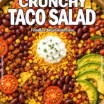 Loaded Crunchy Taco Salad in a large bowl, featuring seasoned ground beef, crisp romaine lettuce, cherry tomatoes, black beans, corn, shredded cheese, thinly sliced avocado, and crushed tortilla chips, with a dollop of sour cream on top. A fresh and vibrant Tex-Mex salad perfect for taco lovers.
