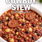 A rich anHomemade Texas-Style Cowboy Stew served in a heavy white bowl on a marble countertop with sausage slices, ground beef, beans, potatoes, corn, and fire-roasted tomatoes, garnished with herbs and a spoon on the side | FoodForYourGood.com