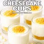 A photo displays four 3-Ingredient No-Bake Cheesecake Cups in clear jars with graham cracker bases, placed on a round marble board garnished with scattered white chocolate chips and a white embroidered towel in the background.