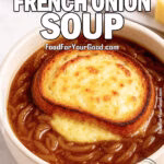 A bowl of Lazy French Onion Soup topped with golden cheese toast, served on a marble countertop with a spoon and cheese blocks in the background.