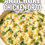 Spinach Artichoke Chicken Orzo in a rustic bowl, with spoon, fresh spinach leaves, and grated cheese in background