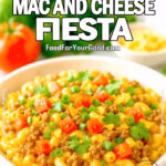 Bright and colorful bowl of taco mac and cheese topped with beef, tomatoes, green onions, cilantro, and tortilla chips, with fresh ingredients in the blurred background.
