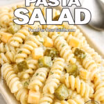 Creamy dill pickle pasta salad with cubed cheddar cheese and chopped pickles served on a white rectangular plate.