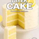 A three-layer Lemon Bliss Layer Cake with cream cheese frosting and lemon slices, served with a slice on a plate in front of the cake on a marble surface.
