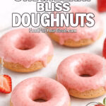 Baked Strawberry Bliss Doughnuts with glossy strawberry glaze, served on a white marble surface with fresh strawberries and a soft white towel in the background.