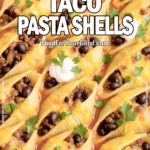Cheesy Taco Pasta Shells baked in a white ceramic dish, topped with melted cheese, sour cream, and chopped green onions on marble.