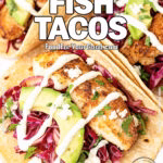 Chili-Lime Fish Tacos on white marble with avocado slices, shredded red cabbage, cotija cheese, and cilantro-lime sauce drizzle.