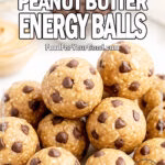 Homemade Chocolate Chip Peanut Butter Energy Balls in slightly varied shapes, stacked on white marble with blurred oats, peanut butter, and chocolate chips in the background.