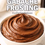 Chocolate Gabache Frosting in a ceramic bowl on white marble with vanilla, butter, and chopped chocolate in background.