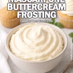 Bowl of Classic Mascarpone Buttercream Frosting with spoon, cupcakes, and fresh ingredients on marble background