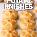 Homemade classic potato knishes on a white marble countertop, golden brown and flaky with potatoes, onion, and herbs in the background.