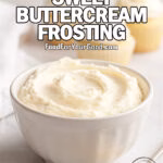Homemade Classic Sweet Buttercream Frosting in a white bowl with a spoonful of frosting and cupcakes in the background on a white marble surface.