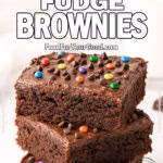 Homemade Cosmic Fudge Brownies with ganache frosting, colorful chocolate pieces, and a glass of milk on white marble