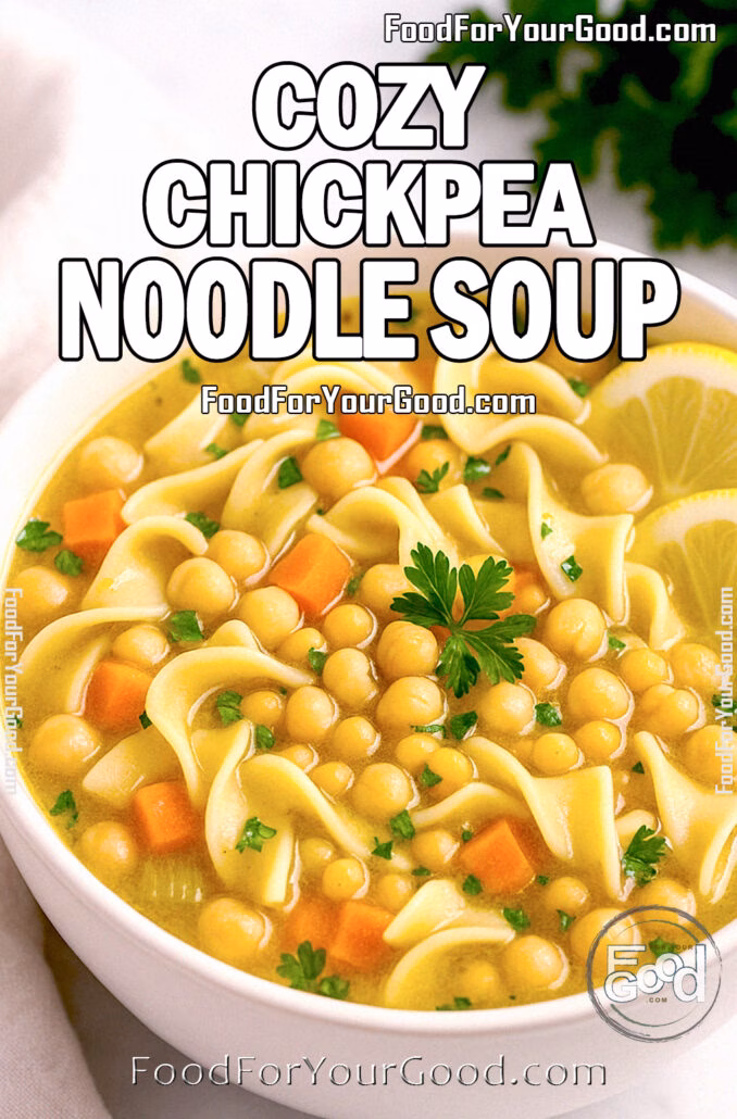 A bowl of Cozy Chickpea Noodle Soup with egg noodles, carrots, chickpeas, and parsley, served with lemon slices on a white countertop.
