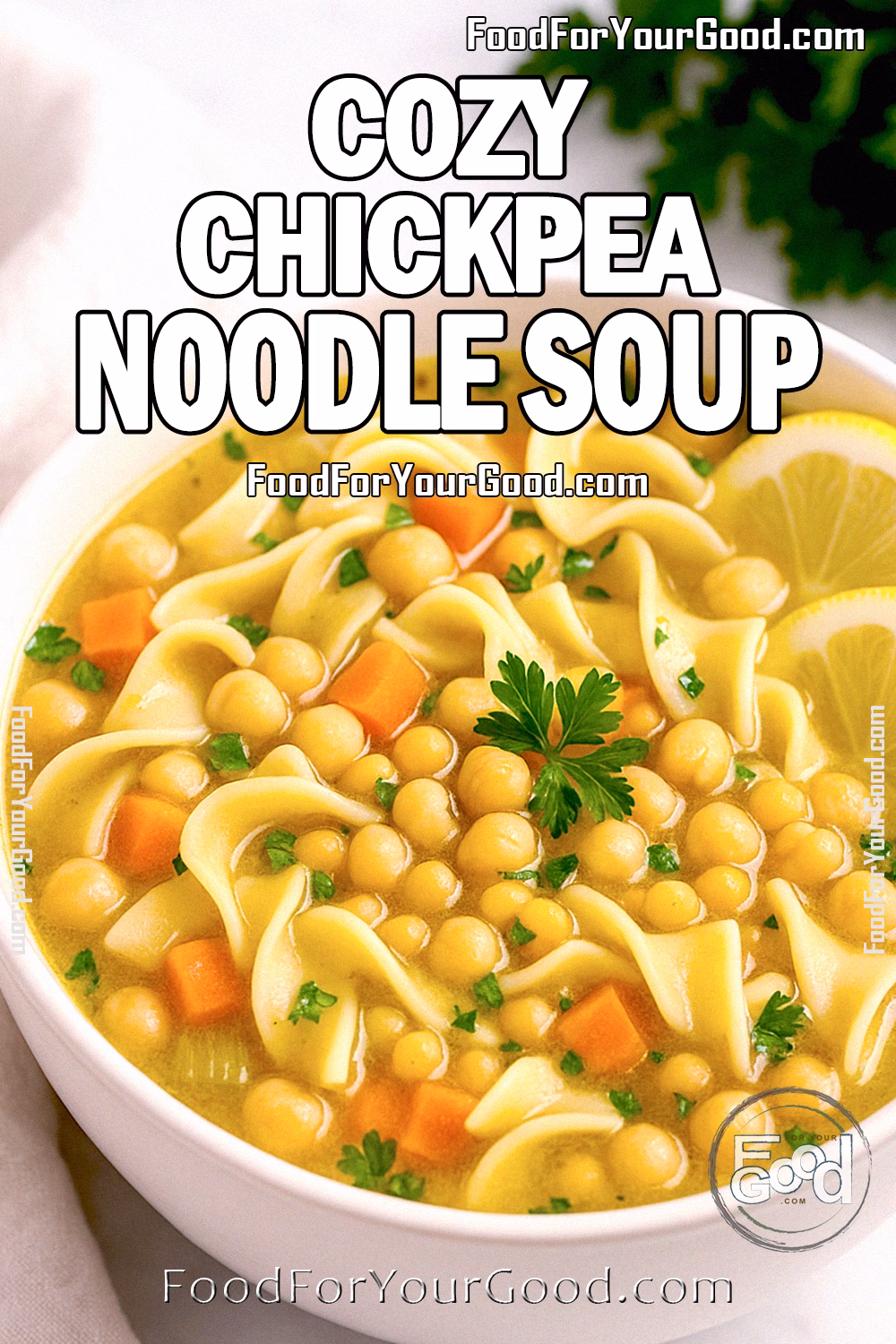 A bowl of Cozy Chickpea Noodle Soup with egg noodles, carrots, chickpeas, and parsley, served with lemon slices on a white countertop.