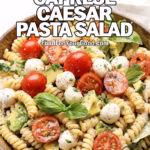 Creamy Caprese Caesar Pasta Salad with rotini, cherry tomatoes, mozzarella, basil, and Caesar dressing served in a rustic bowl on white marble at FoodForYourGood.com