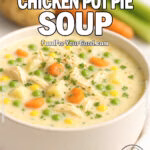 Bowl of creamy chicken pot pie soup with carrots, peas, corn, and potatoes, garnished with fresh parsley, on a white marble background with fresh vegetables in soft focus.