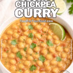 Creamy Coconut Chickpea Curry in a white ceramic bowl, mixed with chickpeas and tomatoes, served with a spoon on a marble countertop.