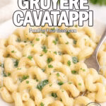 Creamy Gruyère Cavatappi pasta served on a white plate, coated in a thick cheese sauce with spinach and parsley garnish, fork resting in the dish.