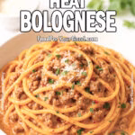 Creamy Heat Bolognese pasta served in a white ceramic bowl, coated in a rich spicy tomato cream sauce, garnished with fresh basil and Parmesan on a white marble countertop.