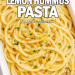 Overhead view of creamy lemon hummus pasta in a white rectangular bowl topped with parsley, pine nuts, and lemon zest