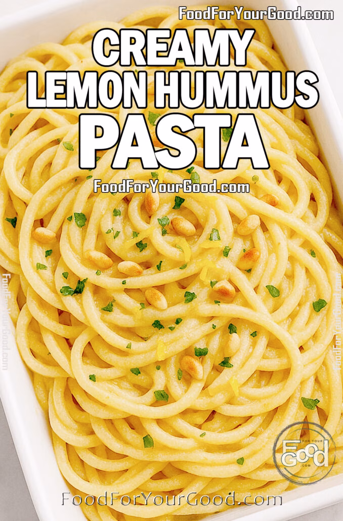 Overhead view of creamy lemon hummus pasta in a white rectangular bowl topped with parsley, pine nuts, and lemon zest