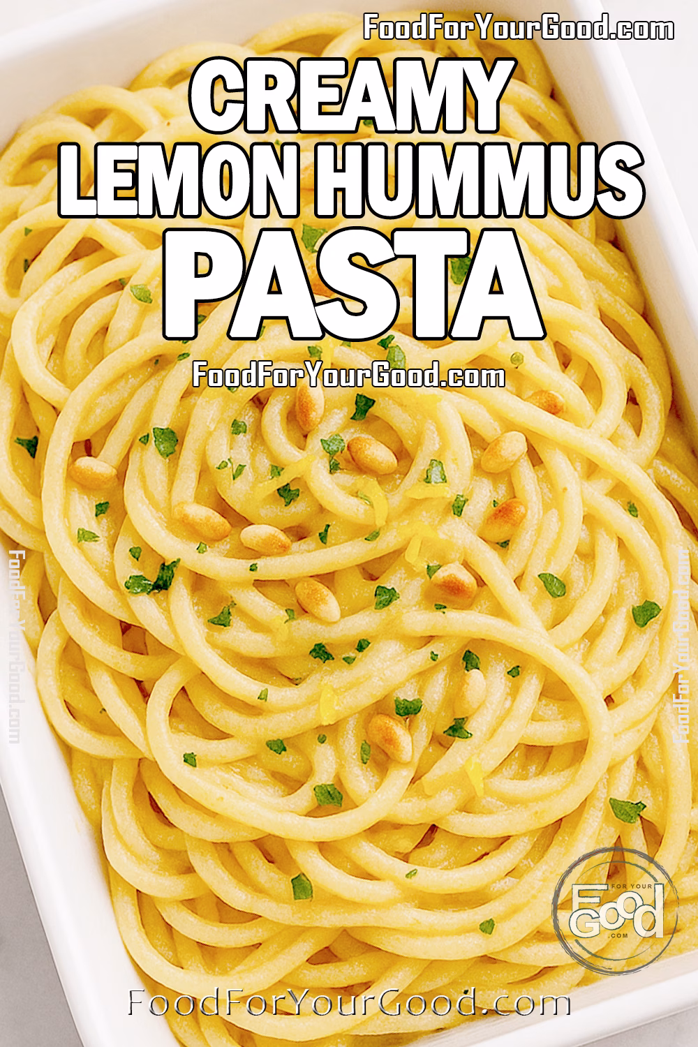 Overhead view of creamy lemon hummus pasta in a white rectangular bowl topped with parsley, pine nuts, and lemon zest