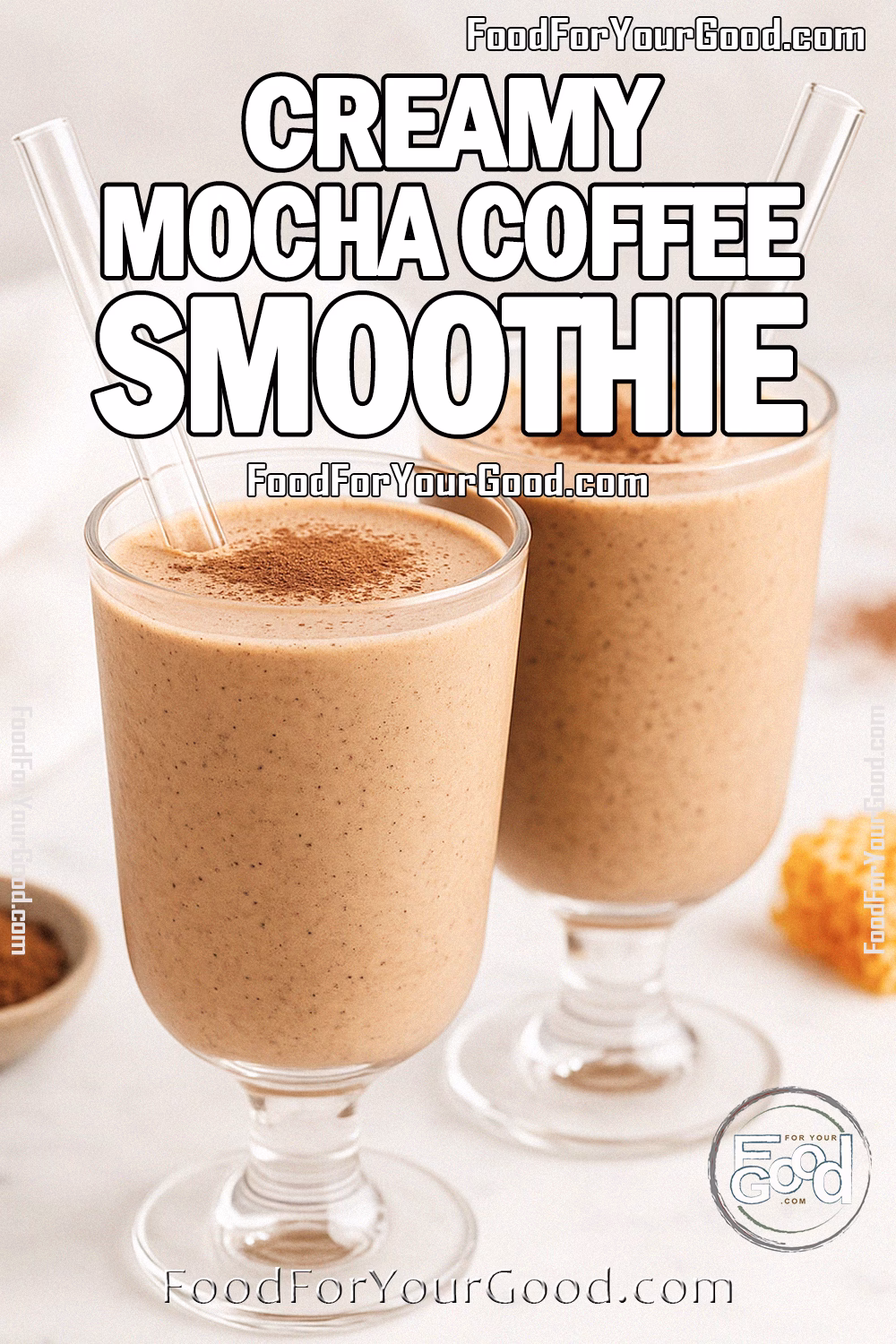 Creamy Mocha Coffee Smoothie in Elegant Glasses – FoodForYourGood.com Two footed glasses filled with creamy mocha coffee smoothie, each with a wide glass straw, set on a white marble surface with cocoa powder, honeycomb, and a white towel in the blurred background.