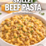 Creamy Skillet Beef Pasta in a white bowl on marble with cheddar, parsley, and onion in background