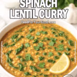 A creamy spinach lentil curry in a white bowl, garnished with cilantro and a lemon wedge, on a marble countertop.
