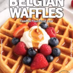 Crisp & Fluffy Belgian Waffles topped with fresh berries, whipped cream, and maple syrup drizzle on a white plate.