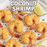 Crispy Air Fryer Coconut Shrimp on a white plate with lime wedges and parsley garnish, set on marble with a white towel in the background.