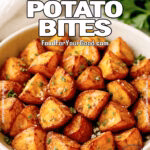 A bowl of Crispy Air-Fryer Potato Bites garnished with parsley and Parmesan on a marble countertop.