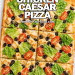 Square Chicken Caesar Salad Pizza topped with romaine, cherry tomatoes, chopped olives, and Parmesan on wrinkled parchment paper.