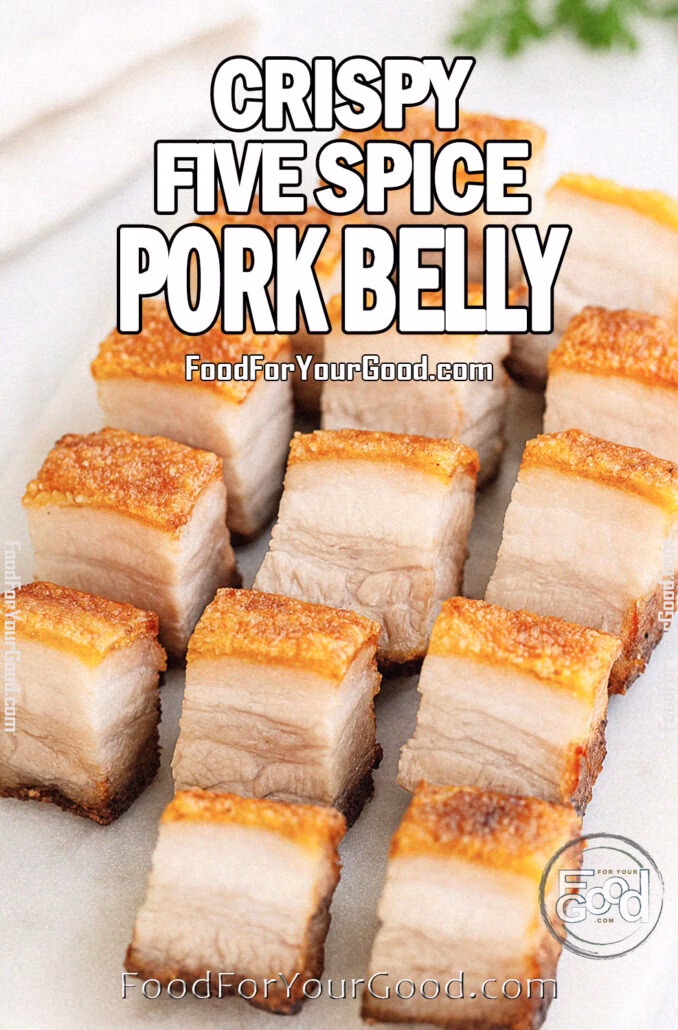 Crispy five-spice pork belly cubes with golden crackling skin arranged on a white marble tray, styled with a white towel and fresh herbs in the blurred background for a rustic, homemade presentation.
