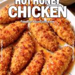 A platter of crispy baked chicken tenders drizzled with golden hot honey glaze, served on a white ceramic plate with a small bowl of hot honey in the background.