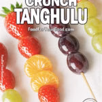 Crystal Crunch Tanghulu skewers with glossy candied grapes, strawberries, and mandarin orange segments arranged on a white marble countertop with a soft blurred towel in the background.