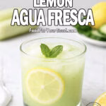 A short, wide glass of Cucumber Lemon Agua Fresca with ice, lemon slice, and a mint sprig on a white marble countertop.