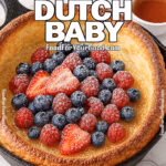 Fluffy Vanilla Dutch Baby in a cast-iron skillet with tall golden edges, topped with fresh strawberries, blueberries, raspberries, powdered sugar, and lightly drizzled maple syrup.