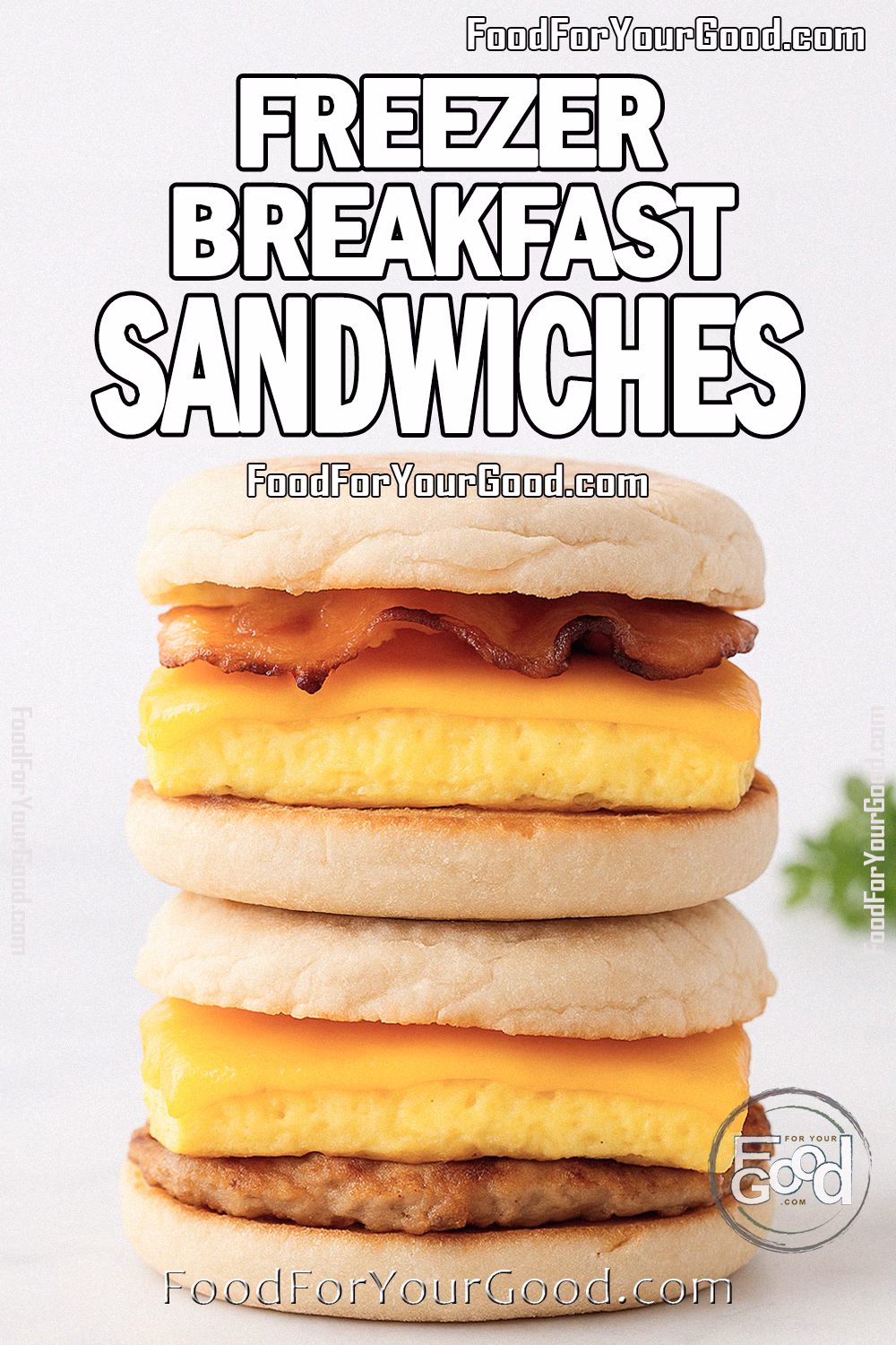 Freezer Breakfast Sandwiches Recipe | FoodForYourGood.com Two stacked Freezer Breakfast Sandwiches on toasted English muffins, filled with baked eggs, melted cheddar cheese, and bacon or sausage. Placed on white marble with a plain white wall background and herbs blurred on the side.