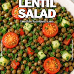 A bowl of French Lentil Salad with cherry tomatoes, cucumbers, red bell peppers, and parsley, served on a white marble surface with a gray towel and fresh parsley in the background.