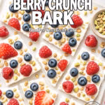 Frozen Yogurt Berry Crunch Bark broken into rustic pieces on a marble tray with parchment paper, surrounded by bowls of fresh berries, granola, and pistachios.