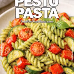 A bowl of Garden Pesto Pasta with roasted vegetables and fresh basil on top, served on a marble countertop.
