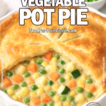 Garden Vegetable Pot Pie in a white ceramic dish with creamy vegetable filling spooned out, on white marble with fresh herbs and veggies blurred in the background.