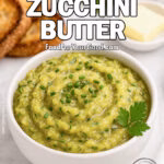 Garden Zucchini Butter in a white ceramic bowl, garnished with chives and parsley, with crispy bread slices and butter on a white marble background.