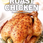 Garlic Butter Roast Chicken on a white plate with herbs, lemon, and garlic on a marble countertop.