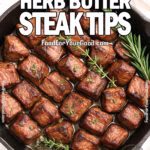Garlic Herb Butter Steak Tips in a black cast iron skillet on a white marble background, featuring varied-sized pieces with tender edges, garnished with rosemary and thyme, and a white towel in the background.