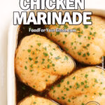 Raw chicken thighs marinating in garlic herb sauce inside a white square ceramic baking dish, placed on a marble surface with a soft white towel